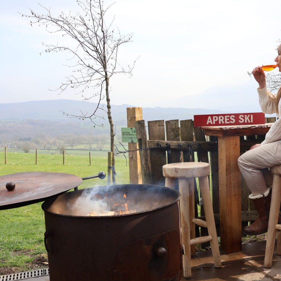 A woman enjoying an Aperol Spritz on the private deck of a luxury glamping pod with scenic views of the Yorkshire Dales.