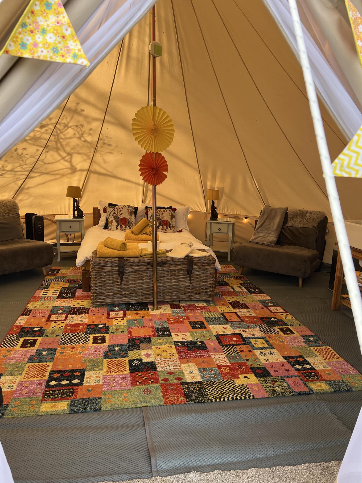 Cosy interior of a luxury bell tent with a double bed, colourful patchwork rug, fairy lights, and rustic decor at Catgill Farm Glamping, Yorkshire.